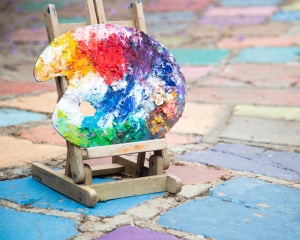 An artist’s palette covered in a rainbow swirl of paints rests on a miniature easel.