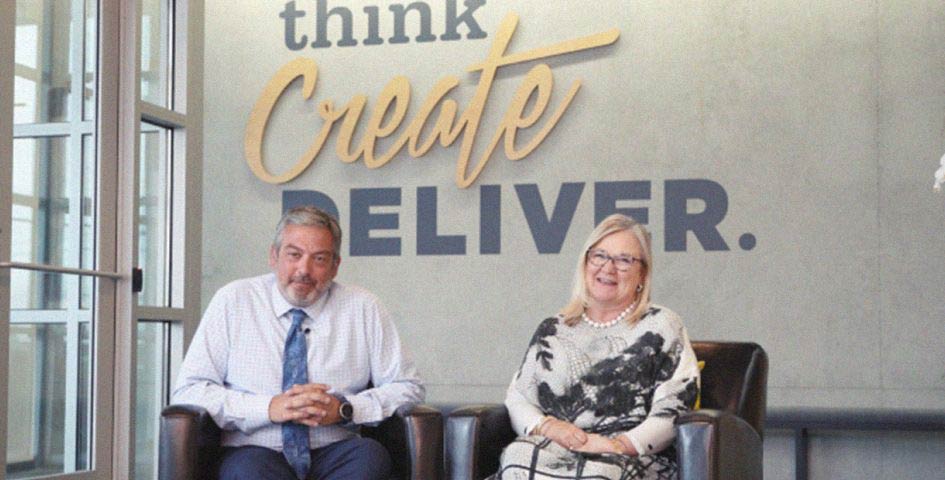 DCG ONE co-founders Brad Clarke and Tammy Peniston, look welcomingly at the viewer in front of a sign that says 'Think. Create. Deliver.'