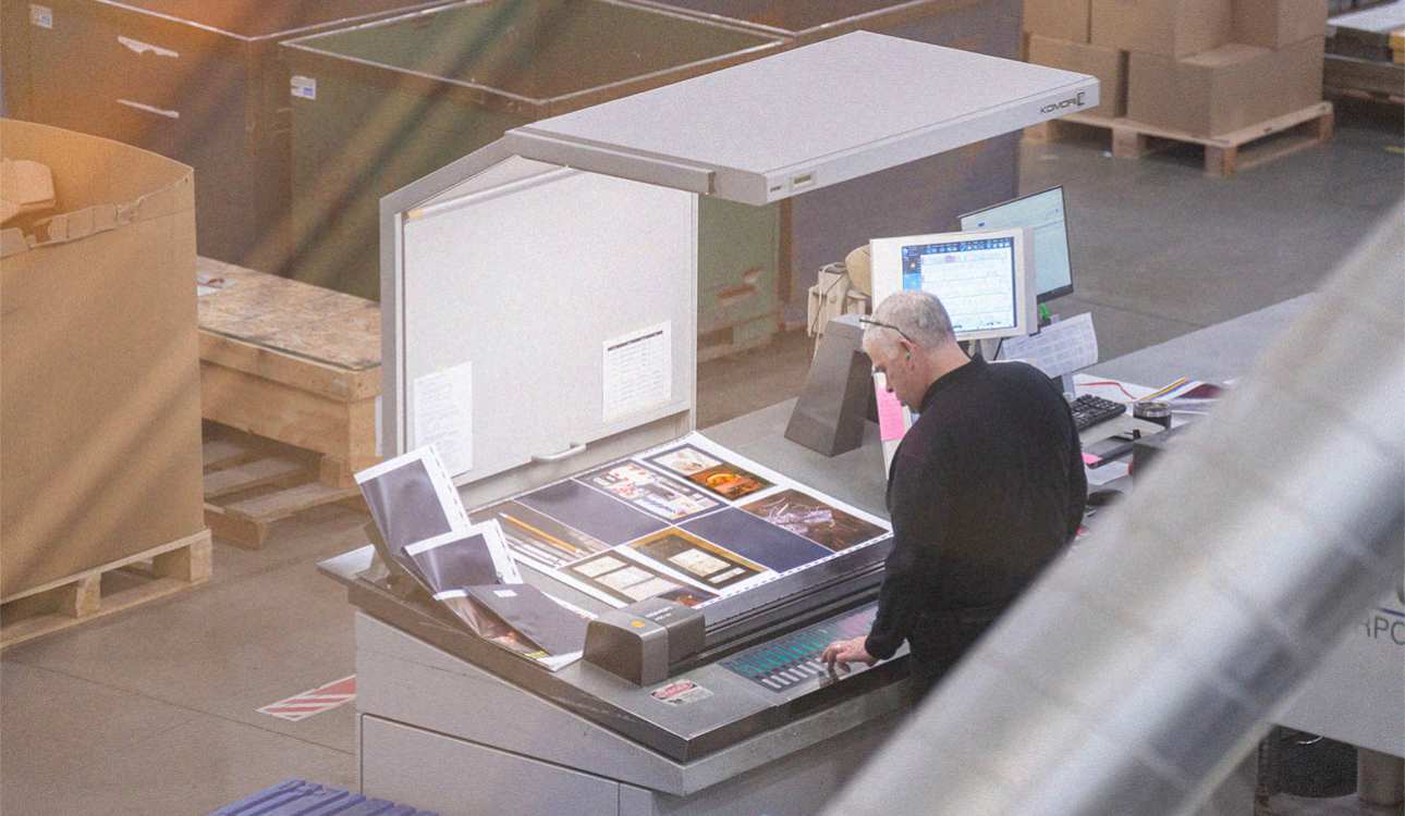 A technician looks at a series of offset print proofs spread on a table under intense light.