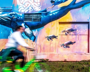 Bikers ride by a colorful mural in a blur, evoking the vibrancy and speed of DCG ONE’s new printer.